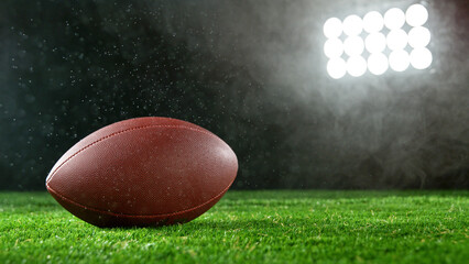 American football ball placed on grass, dark background.