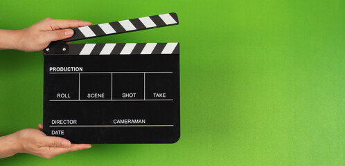 The hands are holding a black clapper board or movie slate on the green screen background.
