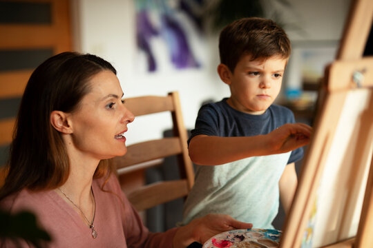 Mother and son painting at home. Little boy drawing with mom in living room..