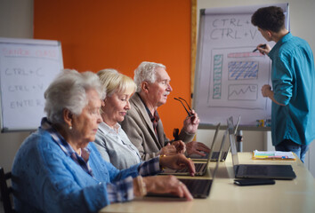 Senior group in retirement home with young instructor learning together in computer class