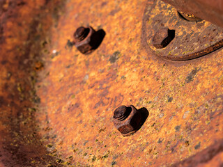 Macro view of a rusty nut on a grungy old bolt on a weathered machinery metal sheet turning orange due to rust and marks of age and deterioration