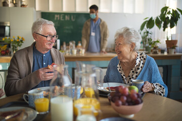Fototapeta na wymiar Smiling elderly woman and man enjoying breakfast in nursing home care center.