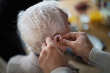 Close-up of caregiver man's hand inserting hearing aid in senior's man ear.