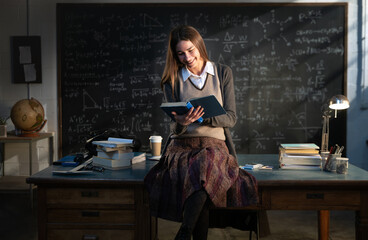 Cinematic shot of young smiling female teacher or student is reading book while sitting on desk in...