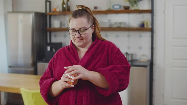 Happy overweight woman take vegetables from fridge for snack in kitchen. Realtime. 