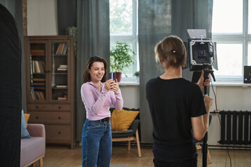 Rear view of assistant adjusting strobe light in living room while blogger shooting video on...