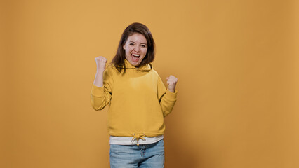 Energetic and ecstatic woman winning enjoying success doing yes hand gesture celebrating victory in studio. Confident casual person smiling cheerful feeling like a winner being happy.