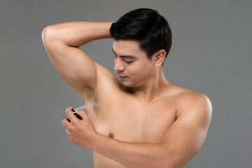 Shirtless handsome man spraying underarm with deodorant in light gray isolated studio background