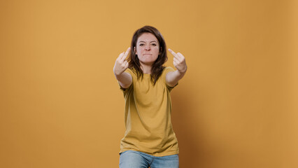 Angry woman showing middle finger obscene hand gesture having aggressive attitude problem being rude and disrespectful in studio. Unhappy person having conflict showing aggresion and anger.
