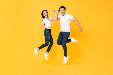 Fototapeta na wymiar Happy energetic smiling Asian couple wearing casual clothes jumping in studio isolated yellow color background