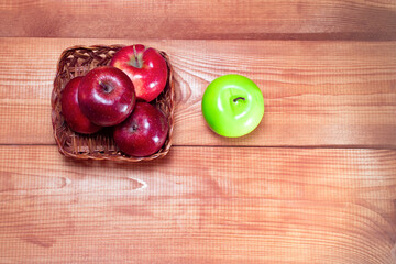 Fresh red apples lie in a wooden basket on a wooden background near one green apple with a place for the text: healthy snack, vitamins, healthy food, ingredients for baking recipes, top view