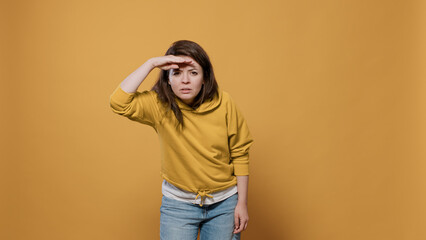 Curious woman looking into the distance far away searching for something with palm over forhead in...