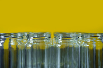 Frontal shot of empty glass jars lined up in a row on a yellow background.