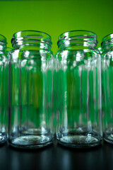 Frontal shot of empty glass jars lined up in a row on a green background. selected focus top of jar in front.