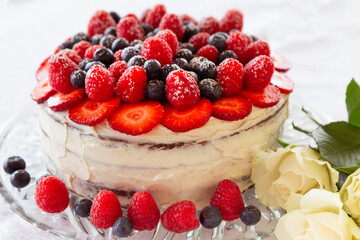 A chocolate and cream naked cake with strawberries, blueberries and raspberries against a white background.