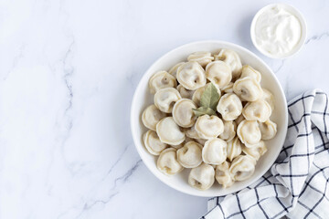 Russian dumplings, pelmeni with meat, sour cream and bay leaf on a marble background, top view, copy space. Selective focus