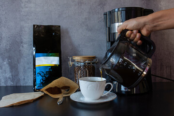 Coffee machine, a cup, a package, a jar full of coffee beans and a spoon of  filter coffee.