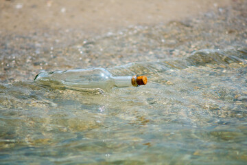 A bottle with a letter thrown out of the sea on a sandy shore.