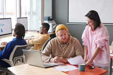 Young brunette woman showing data of analysis to colleague while they working on advertisement campaign