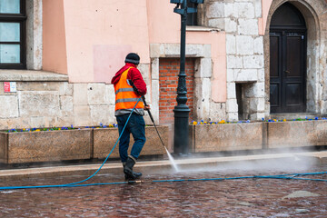 A uniformed worker cleans an area in the city on a rainy morning with a high-pressure cleaner