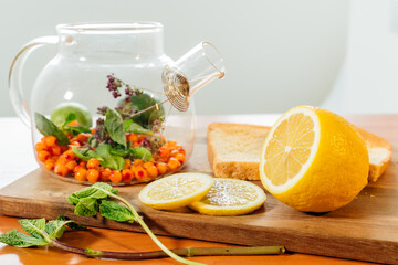 Beautiful glass teapot with sea buckthorn berries, dried thyme and green mint leaves.