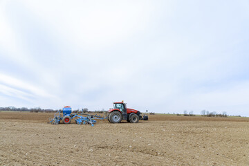 Obraz premium A red tractor with blue equipment sows the field with grain using GPS navigation for precision farming.