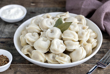 Russian dumplings, pelmeni with meat, sour cream, black pepper,bay leaf on wooden background, side view. Selective focus