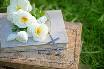old biblical books, Christian cross and rose flowers in garden, green natural background. symbol of...