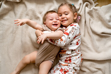 Fototapeta premium cheerful sister and younger brother hugging each other and lying on a blanket, laughing children, lifestyle
