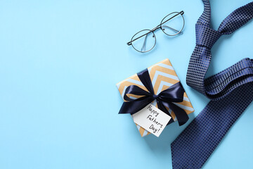 Happy Fathers Day gift box, necktie, glasses on pastel blue background. Flat lay, top view, copy...