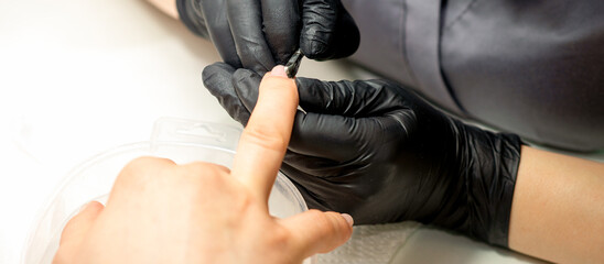 Fototapeta premium Close up professional manicurist master holding customer hand while using a cuticle pusher in a nail salon