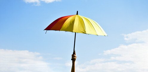 multicolorred umbrella holding in hand in the afternoon of the day, blurr bluesky background.