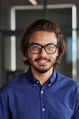 Portrait of smiling successful young mixed race businessman in blue shirt and eyeglasses standing in office