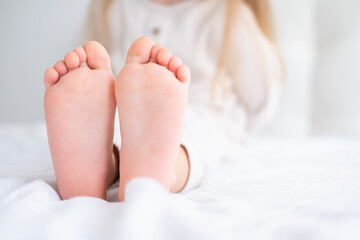 Close up kid child barefooted legs feet lying on white bed linen. Neutral pastel light color tones