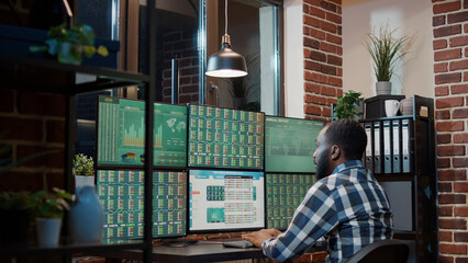 Male financial analyst looking at real time stocks exchange, working at night with multi monitor...