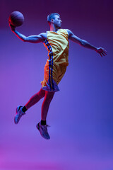 Dynamic portrait of sportive man, basketball player training with ball isolated on purple background in neon light. Goals, sport, motion, activity concepts. © master1305