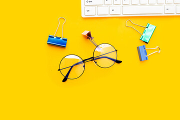 Eye glasses with paper clips and white computer keyboard on yellow background.