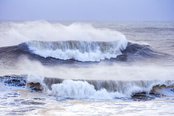 Big waves crashing on the sea with greenish blue color during a cloudy day