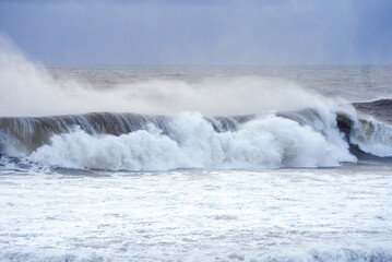 Big waves crashing on the sea with greenish blue color during a cloudy day