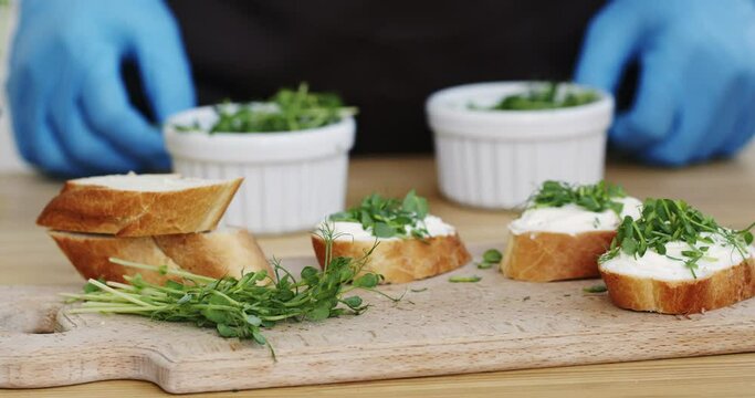 Hands in blue gloves move forward diet sandwiches with microgreens on a wooden board, ready sandwiches for breakfast.