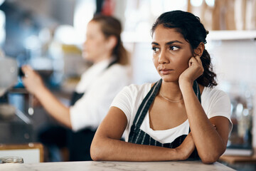 Could a change in career be on the menu. Shot of a young woman looking unhappy while working behind the counter of a cafe. - Powered by Adobe