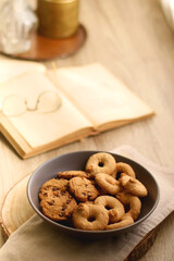 Plate of chocolate chip cookies and sugar cookies, vintage books and reading glasses, candle and flower on the table. Hygge at home. Selective focus.