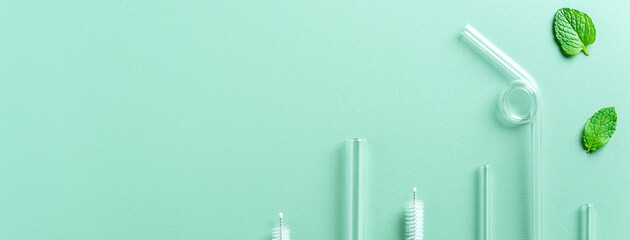 Reusable glass straw and cleaning brush set on green table background.