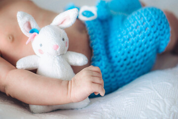 Small baby’s hands holds a toy white rabbit
