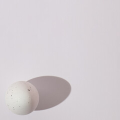White Easter egg on a white background with a sharp shadow with copy space. Minimalistic flat lay scene.