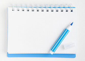 White blank notebook and blue marker on white background. Top view, mockup.