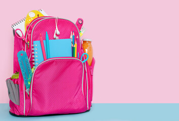 Backpack with school supplies standing on pink background. Copy space.