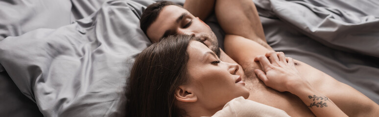Top view of woman lying near muscular shirtless boyfriend on bed, banner.
