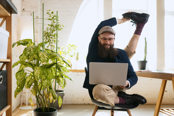 Young bearded man, office clerk having fun, doing yoga on wooden table in modern office at work...