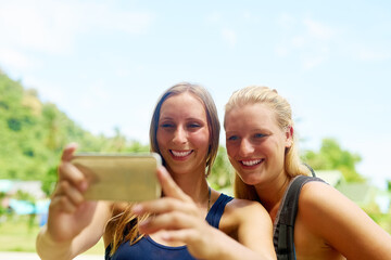 Holiday memories. Cropped shot of two young girlfriends taking selfies on the beach.